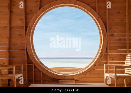 Eine ruhige Inneneinrichtung mit einem großen runden Fenster, das einen atemberaubenden Blick auf das ruhige Meer und die fernen Berge bietet Stockfoto
