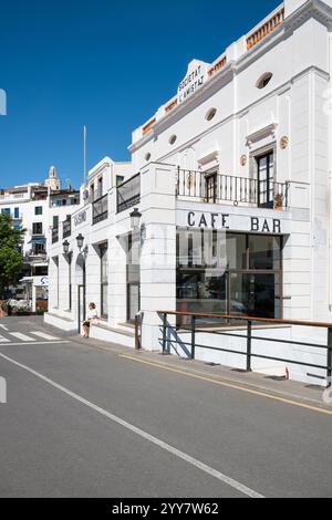 Eine Frau sitzt vor der Casino Bar im Hafen von Cadaqués in der Morgensonne in Katalonien, Spanien Stockfoto
