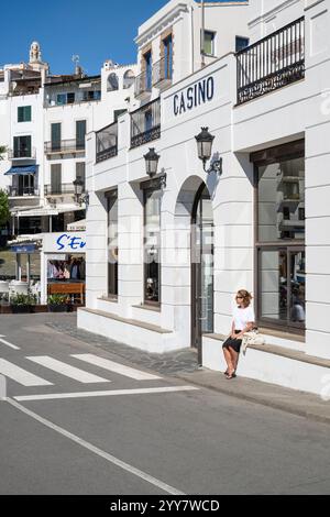 Eine Frau sitzt vor der Casino Bar im Hafen von Cadaqués in der Morgensonne in Katalonien, Spanien Stockfoto
