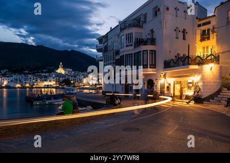 In Cafés sitzen Menschen und schlendern in der Abenddämmerung entlang der beleuchteten Uferpromenade im Hafen und in der Altstadt von Cadaqués, Katalonien, Spanien Stockfoto