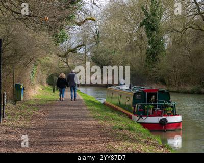 Junge Paare, die Hand in Hand auf einem Kanaltowpfad an einem vertäuten Schmalboot vorbeilaufen, Stoke Bruerne, Northamptonshire, Großbritannien Stockfoto