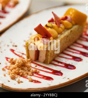 Obstkuchen mit Orangen-, Mango- und Erdbeersauce auf einem weißen Teller Stockfoto