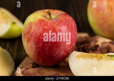 Apfel mit roter und grüner Schale aus nächster Nähe nass und geschnitten, süße, frisch gepflückte Apfelscheiben auf Lärchenbrett, Seitenansicht Stockfoto