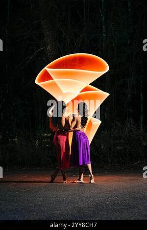 Zwei Frauen in bunten Röcken mit leuchtenden orangen Lichtspuren bei Nacht Stockfoto