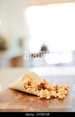 Karamell-Popcorn, das vom Papierkegel auf den Holztisch verschüttet wird. Stockfoto