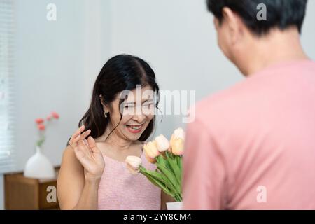 Fröhliches Seniorenpaar feiert Valentinstag mit Blumen und Lächeln in gemütlicher Atmosphäre Stockfoto