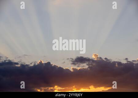 Himmel mit Wolken bei Sonnenuntergang strahlen die Sonnenstrahlen durch die Wolken auf dem Himmelhintergrund während Sonnenuntergang in der Abenddämmerung Stockfoto