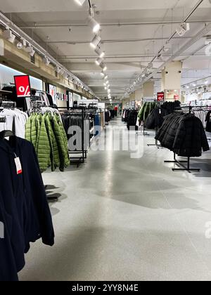 Kiew, Ukraine - 18. Dezember 2024: Hell beleuchtetes Ladeninnere mit Jacken- und Kleiderständern mit Verkaufsschildern. Stockfoto