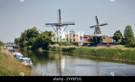 Eine ruhige Szene der Windmühlen Widde Meuln und Bovenrijge in Ten Boer, Groningen, mit einem friedlichen Kanal, Booten und Grün an einem sonnigen Tag. Stockfoto