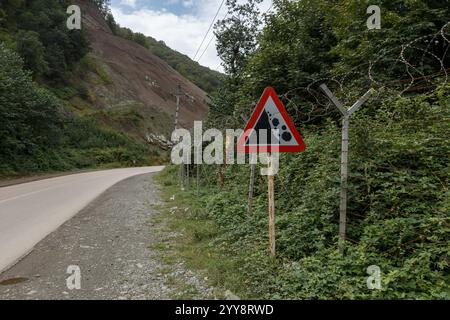 Ein Warnschild warnt Reisende vor möglichen Straßengefahren in der Nähe der Grenze zwischen Iran und Aserbaidschan, umgeben von dichtem Laub und Zäunen. Stockfoto
