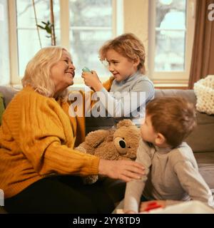 Der Junge untersucht spielerisch den Herzschlag der Großmutter, während das Mädchen Teddybären hält, und kombiniert Lernen mit fantasievollem Spiel, um Gesundheitskonzepte zu verstehen. Stockfoto