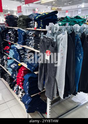 Kiew, Ukraine - 18. Dezember 2024: Regale im Einzelhandel mit verschiedenen gefalteten Kleidungsstücken und ordentlich gehängten Hosen. Stockfoto
