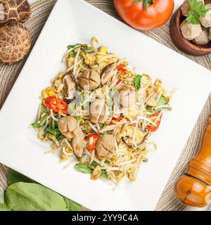 Ein köstliches gebratenes Gericht mit Rindfleischbällchen, Sojasprossen, Pilzen, Eiern und frischem Gemüse, serviert auf einem quadratischen Teller – eine authentische asiatische Mahlzeit Stockfoto