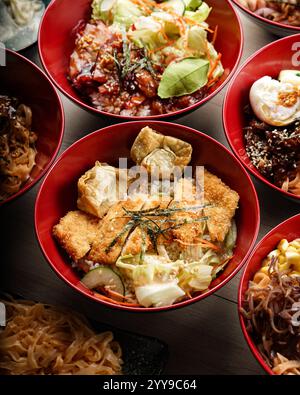 Blick von oben auf eine lebendige asiatische Mahlzeit mit mehreren roten Schüsseln gefüllt mit verschiedenen Reis- und Nudelgerichten, einschließlich gegrilltem Fleisch und Gemüse Stockfoto