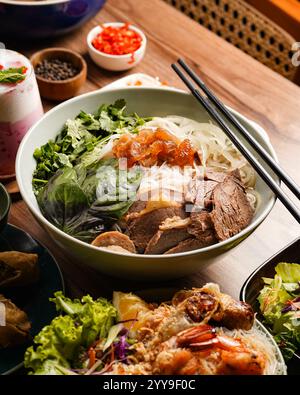 Eine herzhafte Schüssel vietnamesischer Phở Bò Đặc Biệt – duftende Reisnudeln mit seltenem Steak, Brustbrust, Rinderbällchen und Sehne, serviert mit frischen Kräutern Stockfoto