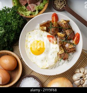 Zarte Rindfleischwürfel, glasiert in herzhafter Sauce, knusprige Knoblauchchips, saftige Tomaten und ein sonniges Ei – alles serviert auf flauschigem Reis. Ein beruhigendes asiatisches Hotel Stockfoto