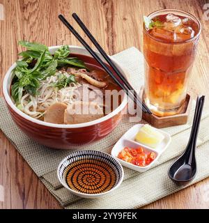 Eine lebendige Schüssel vietnamesischer Fisch und Meeresfrüchte Pho, beladen mit frischen Garnelen, Tintenfischen und Fischkuchen, garniert mit thailändischem Basilikum und Koriander Stockfoto