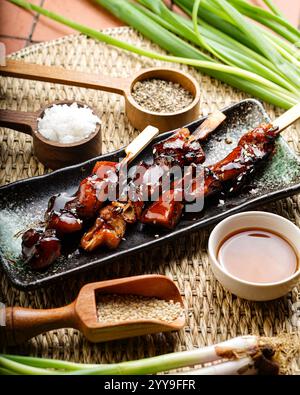 Eine köstliche Portion gegrillter Schweinesieße, perfekt verkohlt und mit kräftigen asiatischen Gewürzen und Beilagen serviert, umgeben von frischen Kräutern Stockfoto