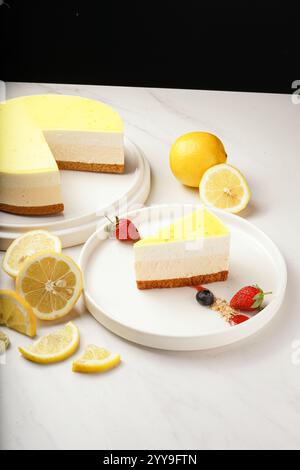 Erfrischender Zitronenkäsekuchen mit einer Kekskruste und einer würzigen Zitronenglasur. Eine Scheibe wird mit frischen Erdbeeren und Heidelbeeren serviert Stockfoto