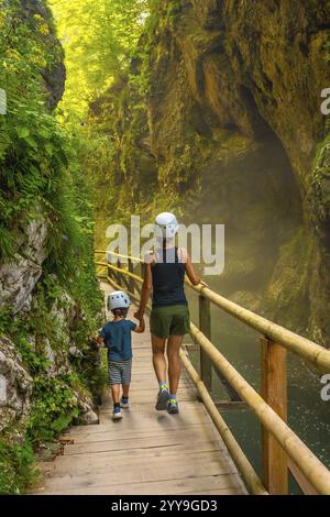 Mutter und Sohn, die Helme tragen, gehen auf einem hölzernen Gehweg und erkunden die wunderschöne vintgar-Schlucht in der Nähe von Bled, slowenien Stockfoto