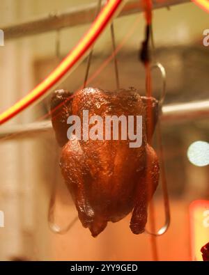 Eine ganze gebratene Ente hängt in einem Schaufenster in einem chinesischen Grillrestaurant, beleuchtet von warmen Neonlichtern, die ihre knusprige Farbe zeigen Stockfoto