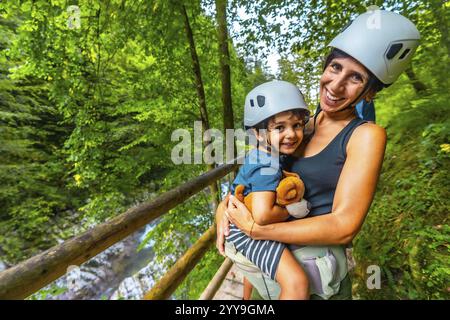 Mutter hält ihren Sohn in der Hand, während sie Helme trägt und genießt die atemberaubende Landschaft der vintgar-Schlucht in Bled, slowenien Stockfoto