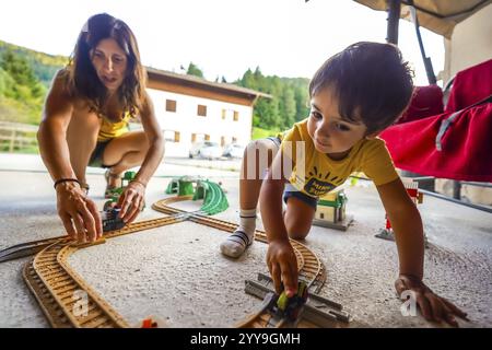 Mutter und Sohn genießen eine gute Zeit zusammen, während sie während ihres Sommerurlaubs mit einem Spielzeugzug auf einer Terrasse spielen Stockfoto