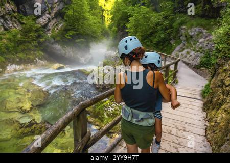 Mutter trägt ihr Kind bei sich, während sie auf einem hölzernen Pfad spaziert und die malerische Schönheit der vintgar-Schlucht in der Nähe von Bled, slowenien, erkundet Stockfoto