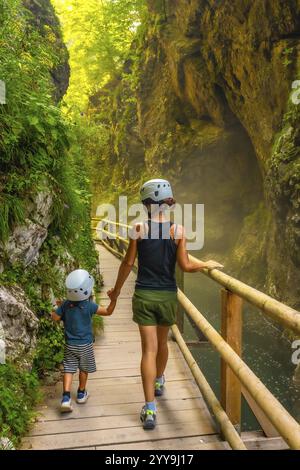 Mutter und Sohn tragen Helme, genießen einen Spaziergang durch die malerische vintgar-Schlucht in slowenien, halten Hände und erkunden gemeinsam die Natur Stockfoto