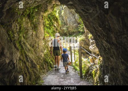 Mutter und Sohn gehen durch eine enge Passage, die in die Felswände der tolmin-Schlucht in slowenien gehauen ist, und genießen einen Sommertag in der Natur Stockfoto