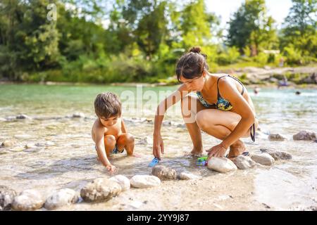 Mutter und Sohn genießen Familienurlaub und spielen an einem sonnigen Sommertag mit Spielzeugautos am Fluss Stockfoto