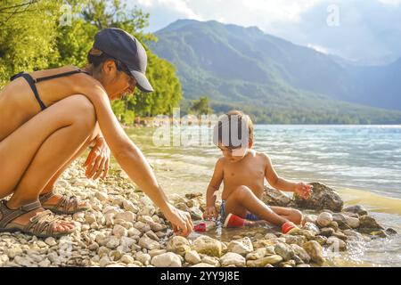 Mutter und Sohn genießen eine gute Zeit zusammen, spielen mit Kieseln und Spielzeugautos am malerischen Ufer des Bohinj-Sees in slowenien Stockfoto