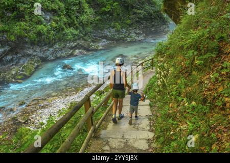 Touristen, die Helme tragen, genießen einen Sommerspaziergang entlang des atemberaubenden türkisfarbenen Flusses radovna, der durch die vintgar-Schlucht in der Nähe von Bled, slowenien fließt Stockfoto