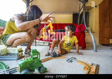 Mutter und Sohn genießen gute gemeinsame Zeit, spielen mit einem Spielzeugzug und einem Kran an einem Sommertag Stockfoto