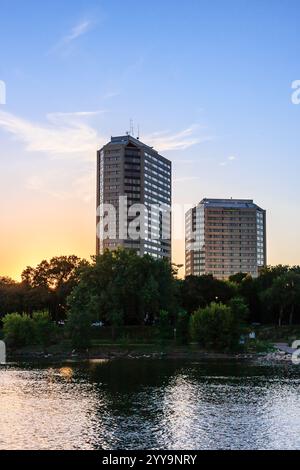 Ein wunderschöner Sonnenuntergang über einer Skyline der Stadt mit zwei hohen Gebäuden im Hintergrund. Das Wasser ist ruhig und spiegelt den Himmel und die Gebäude wider Stockfoto