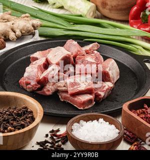 Frische Schweinerippenstücke mit Knochen auf einer gusseisernen Platte, umgeben von aromatischen Gewürzen und Gemüse, perfekt vorbereitet für einen herzhaften hausgemachten Eintopf Stockfoto