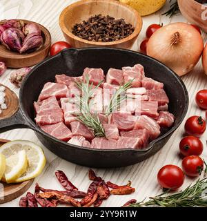 Frische Schweinerippenstücke mit Knochen auf einer gusseisernen Platte, umgeben von aromatischen Gewürzen und Gemüse, perfekt vorbereitet für einen herzhaften hausgemachten Eintopf Stockfoto