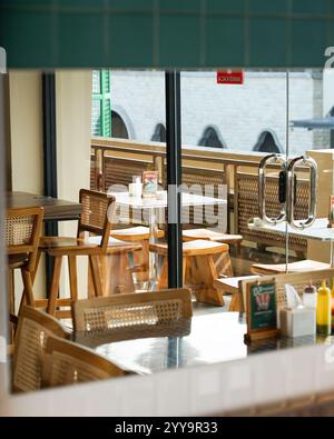Das sonnendurchflutete Innere eines modernen Cafés mit Holz- und Rattanmöbeln, leeren Tischen und Stühlen zum Mittagessen spiegelt ein gemütliches und entspanntes Essen wider Stockfoto