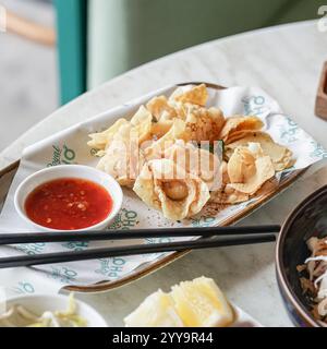 Goldene knusprige Wontons mit Chiliflocken bestäubt, serviert mit süßer und scharfer Dippsauce, serviert mit frischen Chilis und grünen Zwiebeln Stockfoto