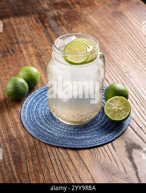 Ein erfrischendes Glas geeisten Calamansi-Saft, serviert in einem einmachglas, garniert mit frischen Limettenscheiben. Auf einem rustikalen Holztisch mit Whole und hal Stockfoto
