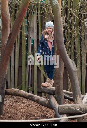 Niedliches kleines Mädchen, das in der kühleren Jahreszeit Spaß auf dem Kinderspielplatz hat Stockfoto