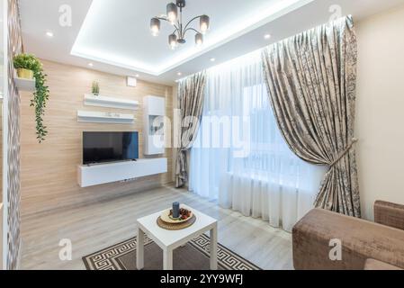 Modern gestaltetes Wohnzimmer mit stilvollen Möbeln, eleganten Vorhängen und beruhigenden neutralen Tönen, die eine perfekte Mischung aus Komfort unterstreichen. Stockfoto