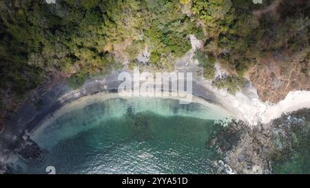 Blick von der Drohne auf eine abgelegene tropische Bucht mit kristallklarem türkisfarbenem Wasser, umgeben von üppig grünen Wäldern und felsiger Küste Stockfoto