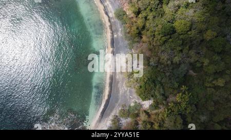 Blick von der Drohne auf eine abgelegene tropische Bucht mit kristallklarem türkisfarbenem Wasser, umgeben von üppig grünen Wäldern und felsiger Küste Stockfoto
