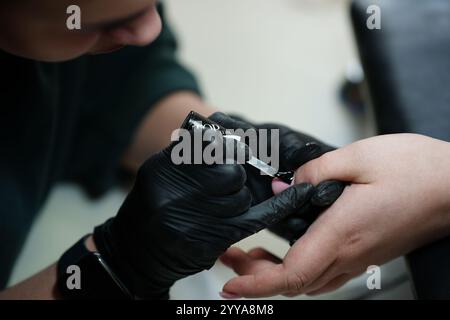 Schönheitsnägel-Konstruktion. Untere Nagelverlängerungen. Meister-Maniküre im Schönheitssalon erhöht die Nägel durch Verlängerung der Nagelplatte des Kunden mit Acryl oder Stockfoto