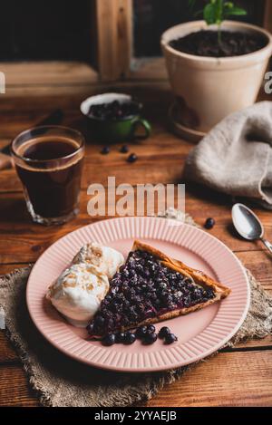 Eine Scheibe frisch gebackener Serviceberry Pie und zwei Kugeln Vanilleeis auf Teller mit einem Glas türkischem Kaffee auf Holztisch Stockfoto