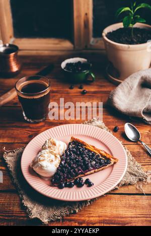 Eine Scheibe frisch gebackener Serviceberry Pie und zwei Kugeln Vanilleeis auf Teller mit einem Glas türkischem Kaffee auf Holztisch Stockfoto