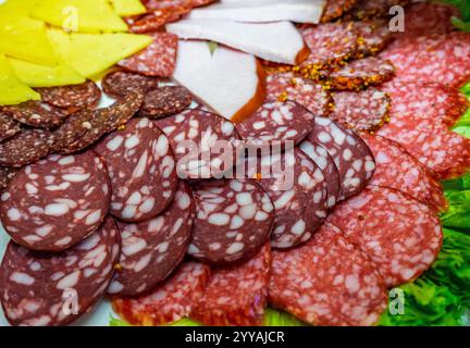 Eine lebendige Platte bietet verschiedene Arten von aufgeschnittenem Fleisch und Käse, die wunderschön auf frischem Gemüse angeordnet sind, perfekt für ein geselliges Treffen oder Feiern Stockfoto