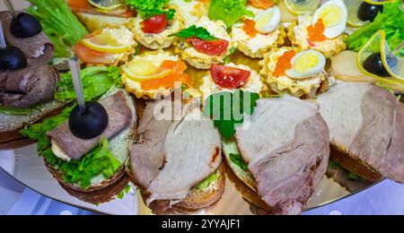 Eine festliche Platte zeigt eine Vielzahl von Gourmet-Sandwiches und eleganten Hors d'oeuvres, wunderschön mit frischen Toppings und Garnituren, perfec Stockfoto