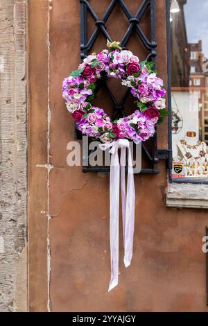 Ein heller Osterkranz aus künstlichen Blumen in Rot- und Pink-Tönen hängt als Dekoration an der Wand des Hauses. Stockfoto